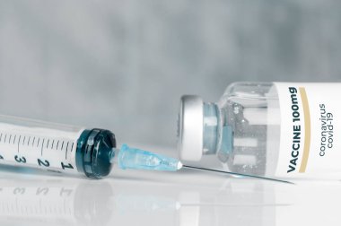 Coronavirus Covid-19 aşısı ve beyaz yansıtıcı bir yüzeyde şırınga.