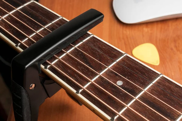 木製のテーブルの上に黒い金属のカポを持つアコースティックギター — ストック写真