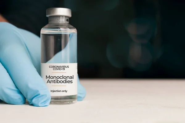 Doktor, beyaz bir masada bir şişe monoklonal antikor, Coronavirus Covid-19 için yeni bir tedavi tutuyor.