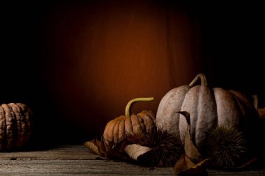 Kabaklar ve kestane yaprakları turuncu arka plandaki ahşap bir masada, bir sürü kopya alanı