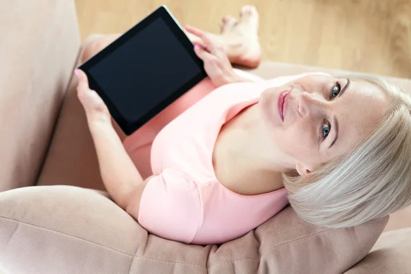 Leende vackra medelålders kvinna sitter på soffan med en tablett, med tanke på ny idé. — Stockfoto