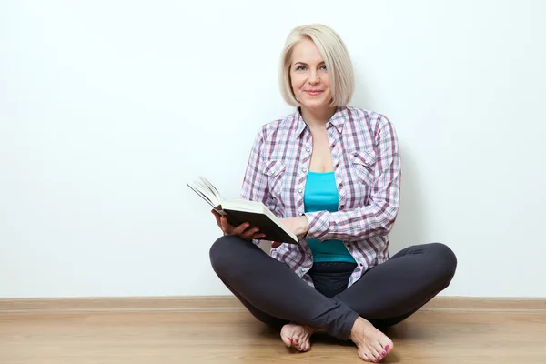 Vrouw thuis zittend op de vloer ontspannen en boek lezen. — Stockfoto