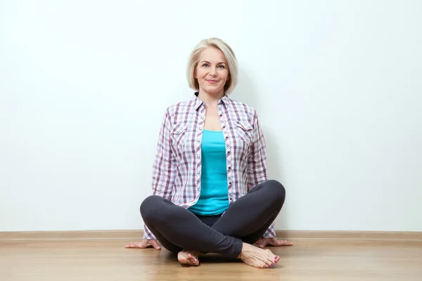 Mujer feliz sentada en el suelo con las piernas cruzadas en ropa de moda sobre fondo blanco en el estudio — Foto de Stock