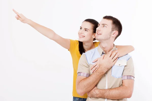 Jeune femme et homme avec un sourire blanc parfait dans les vêtements d'été montre les points avant les doigts de côté sur l'espace vide sur le mur blanc. — Photo