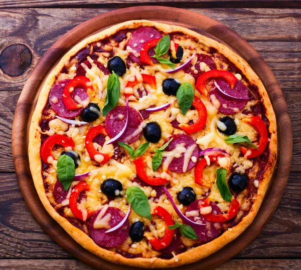 与火腿、 辣椒和橄榄的披萨。美味的新鲜披萨送达木制的桌子上. — 图库照片