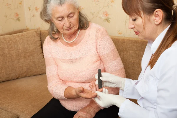 Verpleegkundige neemt test voor suiker in het bloed van oudere vrouw thuis. — Stockfoto