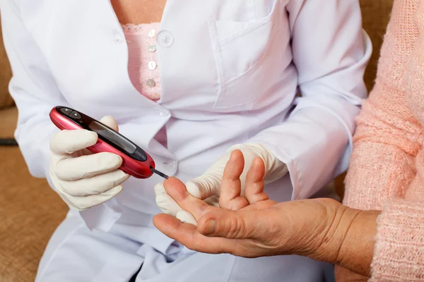 Verpleegkundige neemt test voor suiker in het bloed van oudere vrouw thuis. — Stockfoto