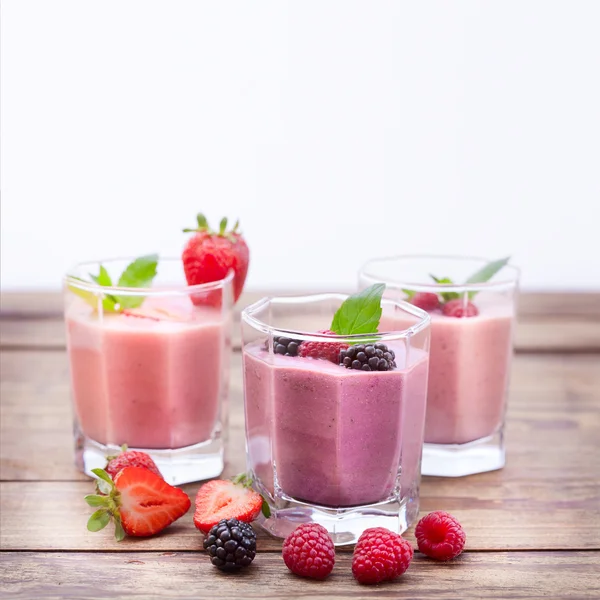 Vypít čtyři letní jahodový koktejly, blackberry, kiwi, maliny na dřevěný stůl. — Stock fotografie