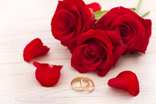 Wedding rings and wedding bouquet of red roses petals. — Stock Photo, Image