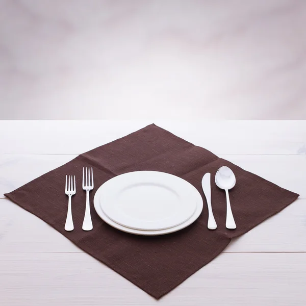 Empty plates and cutlery tablecloth on wooden table for dinner. — Stock Photo, Image