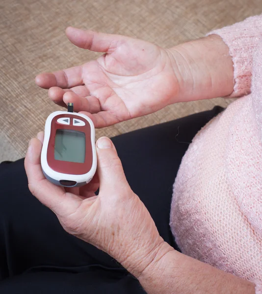 Medicine, diabetes, glycemia, health care and people concept - close up of woman checking blood sugar level by glucometer and test stripe at home — Stock Photo, Image