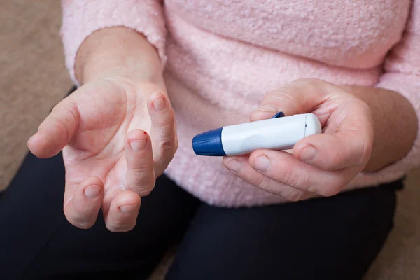 Medicine, diabetes, glycemia, health care and people concept - close up of woman checking blood sugar level by glucometer and test stripe at home — Stock Photo, Image