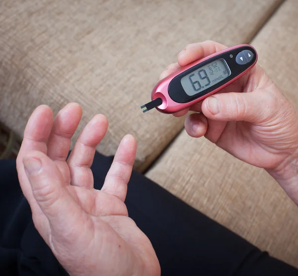 Medicine, diabetes, glycemia, health care and people concept - close up of woman checking blood sugar level by glucometer and test stripe at home — Stock Photo, Image