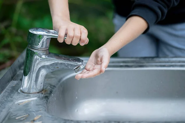 Parkta ellerini yıkayan bir kız. Bebeğim musluğu kapatmaya çalış. Bir çocuğun eli musluğu kapatıyor. Su tasarrufu. Dünya Su İzleme Günü. Çevre ve sağlık konsepti. Yeşil arkaplan