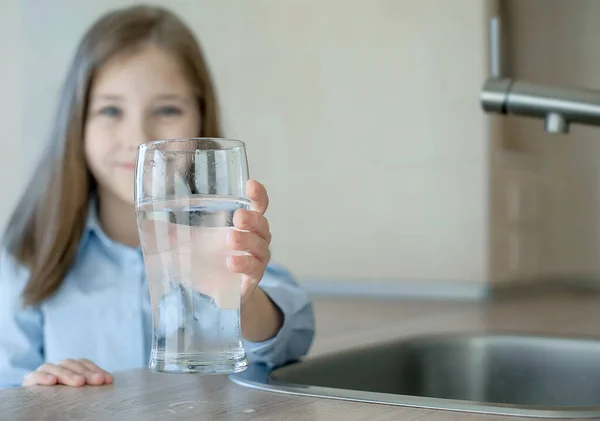 Bir bardak su tutan mutlu küçük kız. Ön planda bir bardak suyla çocuk eline odaklan. Sıvı kaybı. Su kalitesi kontrolü. Dünya Su İzleme Günü. Çevre kirliliği sorunu