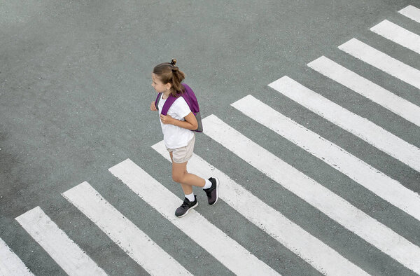 Schoolgirl crossing road on way to school. Zebra traffic walk way in the city. Concept pedestrians passing a crosswalk. Stylish young teen girl walking with backpack. Active child. Top view