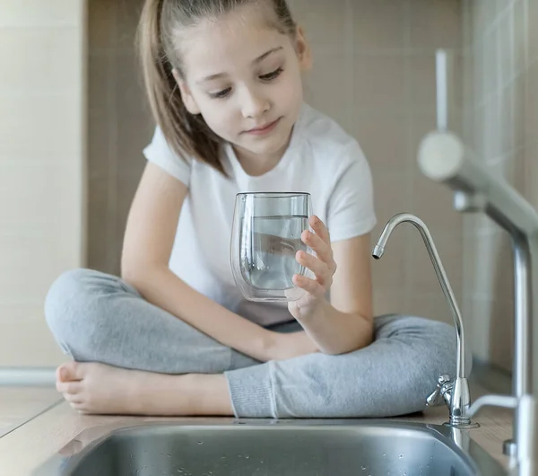 Küçük çocuk camdan taze ve saf musluk suyu içiyor. Mutfak musluğundan bardağa su dökülüyor. Sıfır israf ve plastik bilinçli minimalizm yaşam tarzı konsepti yok. Çevre ve ekoloji
