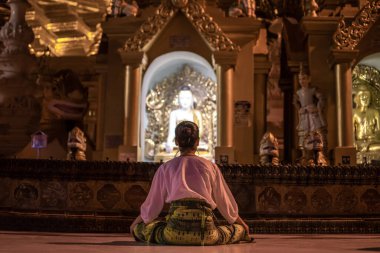 Yangon, Myanmar - 30 Aralık 2019 Bir kadın Shwedagon Pagoda 'daki bir Buda heykelinin önünde dua ediyor ve meditasyon yapıyor.