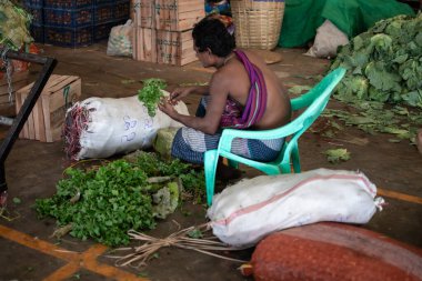 YANGON, MYANMAR - 31 Aralık 2019: Plastik bir sandalyede oturan genç bir burmalı yeşil sebze yapraklarını sıralıyor