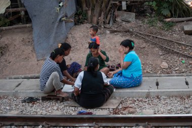 YANGON, MYANMAR - 31 Aralık 2019: Yangon 'un dışındaki demiryolu raylarında beş yerli kadın oyun oynuyor, bir çocuk geçiyor