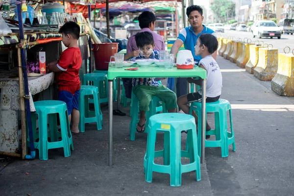 YANGON, MYANMAR - 1 Ocak 2020: Burmalı bir aile Yangon 'un merkezindeki kalabalık caddenin yanındaki bir gıda standında kahvaltı ediyor