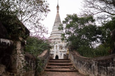BAGAN, NYAUNG-U, MYANMAR - 2 HAZİRAN 2020: Eski bir tuğla geçidinin arkasında beyaz bir Budist pagoda stupa