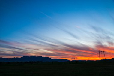 Gün batımı gökyüzü ve elektrik kuleleri ile tarlanın üzerinde bulutlar