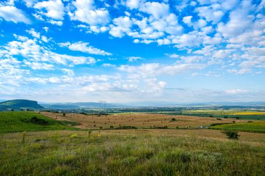 Kurumuş saman ruloları ve bulutlu mavi gökyüzü ile tarım arazisi, elektrik voltaj direkleri 