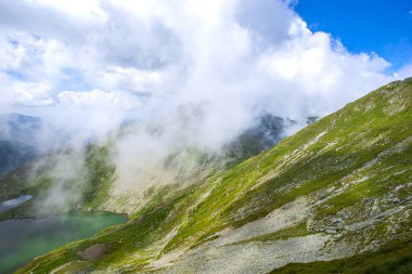 Görkemli dağlar, bulutlu gökyüzü, tepeler arasında göl suyu. 