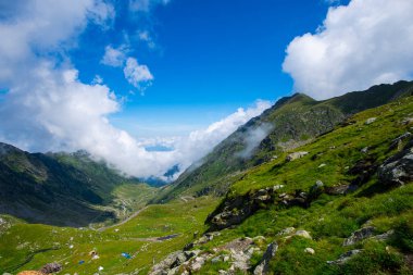 Yeşil çimen tepeleri ve mavi gökyüzünde bulutlu dağlar 