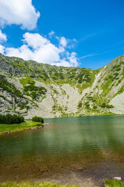 Görkemli dağlar, bulutlu gökyüzü, tepeler arasında göl suyu. 