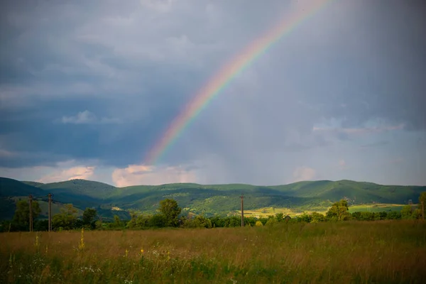 view of field of mountains and rainbow in sky