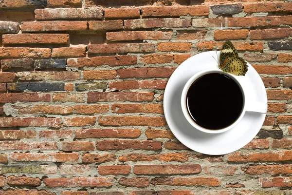 Taza de café y mariposa sobre fondo de ladrillo rojo — Foto de Stock