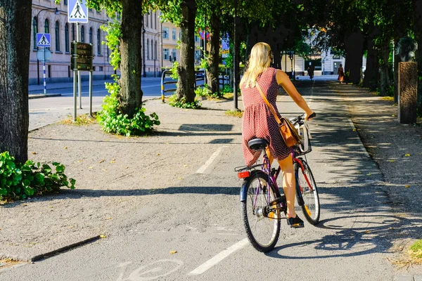 Woman rides a bicycle on a bike lane in Sweden. Girl is riding her bike on the path to Stockholm center.