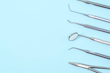 Açık mavi arka plandaki dişçi araçları: kornzange, curette, diş sondası, brüt-mayer klemp, diş aynası ve kaşifler. Diş sağlığı ve sağlık hizmetleri kavramı.
