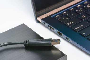 Yakınlarda USB 3.0 kablosu ve dizüstü bilgisayarı olan harici bir sabit disk. Taşınabilir kaputtaki veri depolama kavramı. Gölgeli beyaz yüzeye yakın çekim.