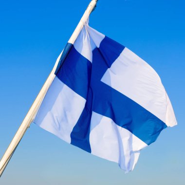 Finlandiya bayrağı açık mavi gökyüzüne karşı rüzgarda dalgalanıyor.