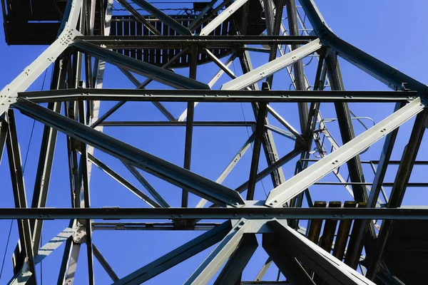 Metal industrial construction of a port crane against the deep blue sky, bottom view.