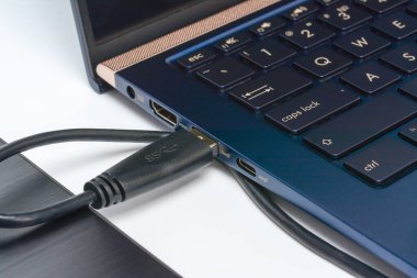 USb 3.0 kablosu ile laptopa bağlı harici disk diski. Taşınabilir kaputtaki veri depolama kavramı. Gölgeli beyaz yüzeye yakın çekim.