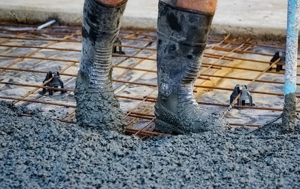 İşteki bir adam ıslak betona çizmeli bacaklara beton döküyor.