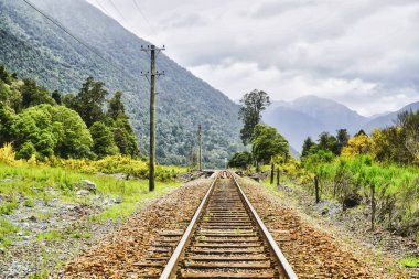 Yoğun yeşil orman, bulutlu gökyüzü, seyahat, yalnızlık, macera ve sessiz doğal güzellikleri çağrıştıran yemyeşil bir dağ vadisine uzanan tek bir demiryolu hattı var. Otira Yeni Zelanda