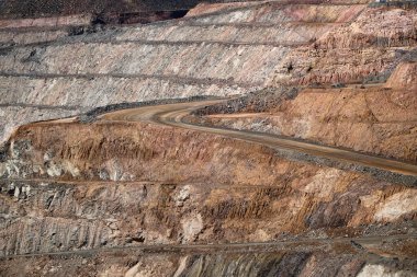 Katmanlı teras bankları ve kahverengi kaya ve toprağa oyulmuş kazı alanı, jeoloji ve endüstriyel çıkarmayı gösteren kıvrımlı bir yol gösteren devasa bir açık çukur mayını.
