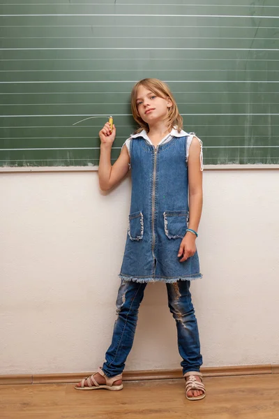 Schoolgirl standing in front of the chalkboard in the school. — Stock Photo, Image