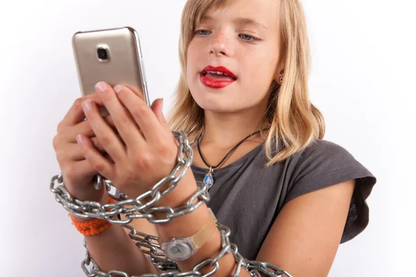 Chica joven encadenada con una cadena usando un teléfono inteligente . — Foto de Stock