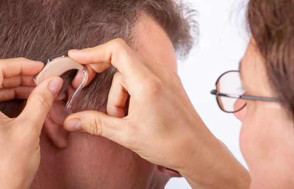 Doctor fitting a senior man patient with hearing aid — Stock Photo, Image