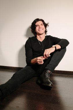 Genç adam sırtını duvara ile yere oturur.