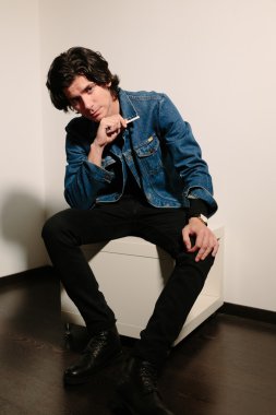 Genç adam bir sigara elinde tutan ve Osmanlı üzerinde oturur.