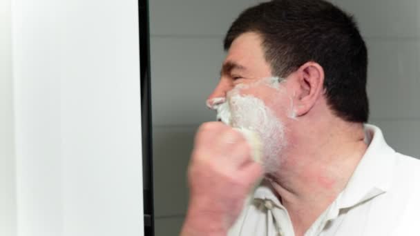 O homem põe uma nata de cara por meio de uma pequena escova tem uma barba então . — Vídeo de Stock