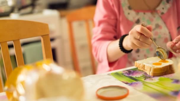 Camera van links naar rechts beweegt en verwijdert hoe de jonge vrouw kookt voor zichzelf zoete broodje van jam. — Stockvideo