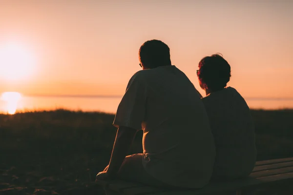 Vista lateral de una pareja casada una silueta sentada en un banco . — Foto de Stock